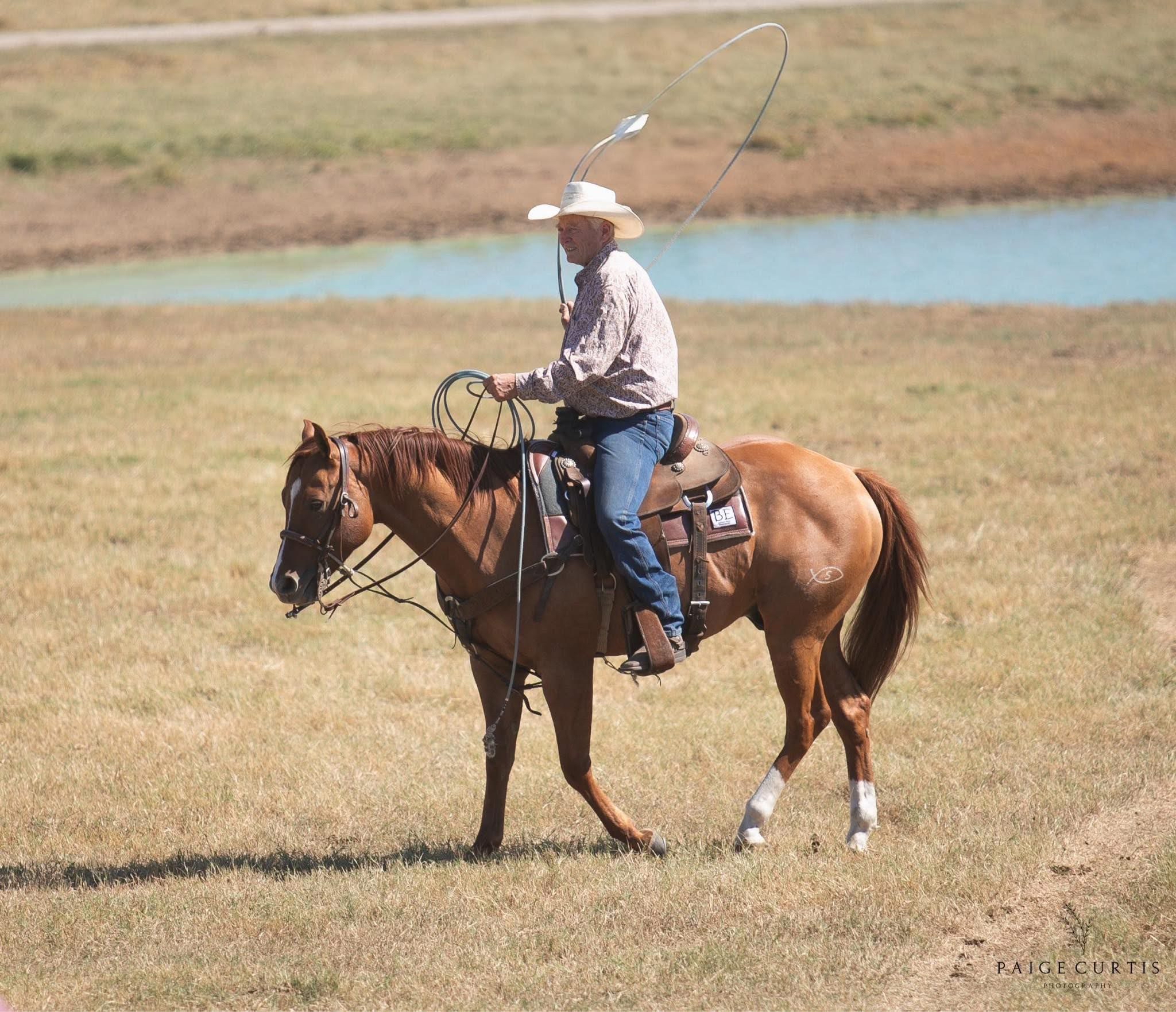 Kelly Smallwood horseback with a rope in an open pasture.